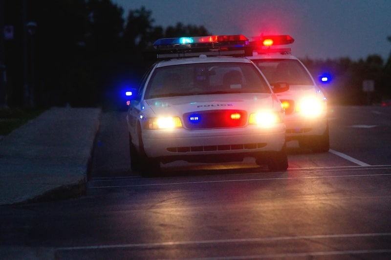 Two white police cars with flashing red and blue emergency lights parked on a road at night.