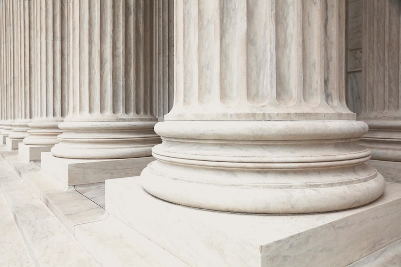 Close-up of the bases of white marble fluted columns of a classical building, symbolizing law, justice, or government architecture.