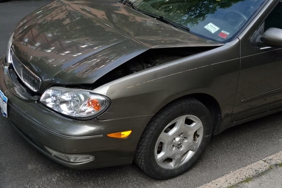 Close-up of a grey sedan with front-end damage, showing a crumpled hood and misaligned bumper after a car accident.