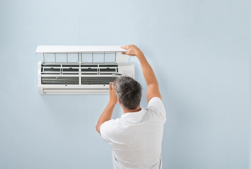 A technician in a white shirt performing maintenance or cleaning on a wall-mounted split air conditioning unit.