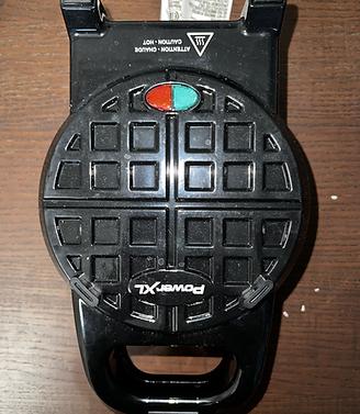 Top-down view of a closed black PowerXL Stuffed Wafflizer on a wooden surface with red and green indicator lights.