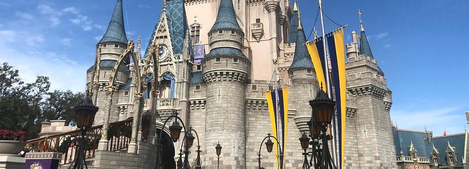 Cinderella Castle at Walt Disney World Resort with blue turrets, gold accents, and yellow and blue banners under a bright sky.