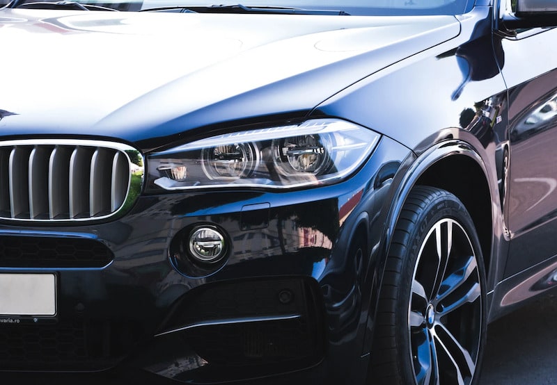 Close-up of the front-left profile of a dark navy blue BMW SUV, highlighting the sleek design of its signature kidney grille, LED headlight assembly, and alloy wheel.