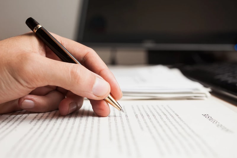 Close-up of a person's hand holding a black and gold pen while reviewing or editing a printed business report on a desk.