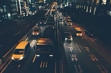 High-angle view of city traffic on a multi-lane highway at night with illuminated vehicle headlights and Japanese road markings.