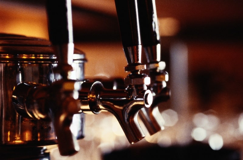 Close-up of polished chrome beer taps in a dimly lit bar, with a warm, bokeh background of lights.