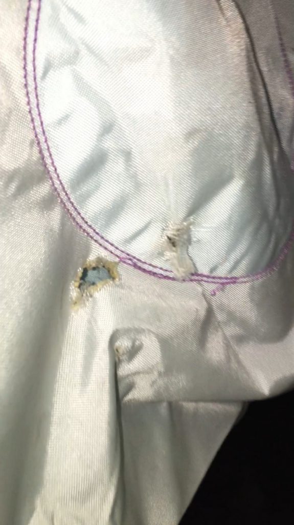 Close-up of a small hole and frayed damage on white fabric with purple stitching, likely from a product defect or wear.